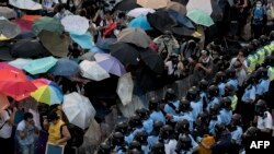China/Hong Kong -- Pro-democracy protesters hold umbrellas and wear protective clothing in front of a police line near the government headquarters in Hong Kong on September 28, 2014