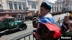 Un copil surprins în timp ce urmărește parada militară de Ziua Victoriei, care marchează cea de-a 78-a aniversare a victoriei asupra Germaniei naziste în cel de-al Doilea Război Mondial, în Vladivostok, Rusia, 9 mai 2023.