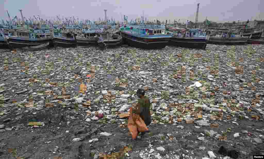 A Pakistani boy looks to collect recyclable items among the polluted waters in front of fishing boats at Karachi Fish Harbor. (Reuters/Akhtar Soomro)