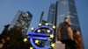 Dy persona me maska kalojnë pranë një shenje të euros të vendosur pranë selisë së Bankës Qendrore Evropiane. Fotografi nga arkivi. 
