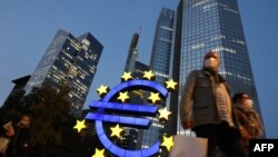 Prolaznici ispred znaka evra kod bivšeg sedišta ECB u centru Frankfurta na Majni, 21. oktobar 2020.