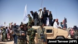 FILE: Afghan Taliban militants and residents stand on a armored Humvee vehicle of the Afghan National Army (ANA) as they celebrate a ceasefire on the third day of Eid in Maiwand district of Kandahar province on June 17.