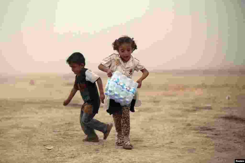 An Iraqi girl, who fled from the recent violence in Mosul, carries a case of water at a camp on the outskirts of Irbil, in the Kurdistan region on June 12. (Reuters)