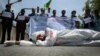 An Afghan man wearing clothes spattered in red color lays down on a road as protesters shout slogans against the Iranian regime and demand justice during a protest outside the Iranian Embassy in Kabul, May 7, 2020