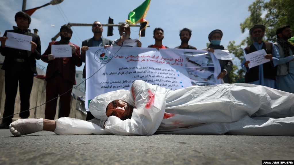An Afghan man wearing clothes spattered in red color lays down on a road as protesters shout slogans against the Iranian regime and demand justice during a protest outside the Iranian Embassy in Kabul, May 7, 2020