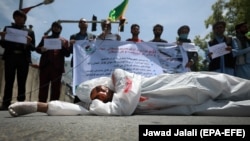 An Afghan man wearing clothes spattered in red color lays down on a road as protesters shout slogans against the Iranian regime and demand justice during a protest outside the Iranian Embassy in Kabul, May 7, 2020