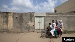 A family rides past the locked house of a Christian girl accused of blasphemy, on the outskirts of Islamabad.