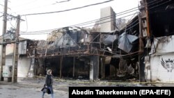 An Iranian woman walk past next to a shopping center that was burned during the protests over increasing fuel price by government in city of Shahriar, Alborz province, November 20, 2019