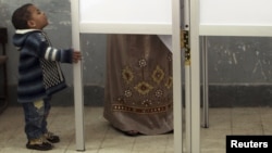Ребенок смотрит, как его мать голосует на выборах в Египте в 2012 году