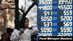 Прохожая рядом с табло с курсом покупки и продажи иностранной валюты. Алматы, 9 марта 2020 года.