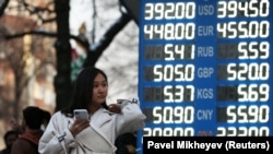 Девушка со смартфоном у электронного табло пункта обмена валют. Алматы, март 2020 года.