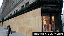 O femeie trece pe lângă un magazin Saks Fifth Avenue din New York la 1 noiembrie 2020. Vitrinele către stradă ale magazinului au fost acoperite cu scânduri pentru a prevenit posibilele atacuri, furturi și vandalizarea magazinului.