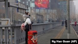Пекин көшесінде тұрған жолаушы. Анадайдан вируспен күресуге үндеген партияның плакаты көрінеді. Қытай, 13 ақпан 2020 жыл.
