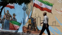 An Iranian man walks next to a mural on a street in Tehran on May 11.