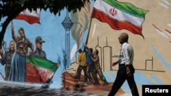 An Iranian man walks next to a mural on a street in Tehran on May 11.