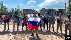 Într-o captură preluată dintr-un videoclip și difuzată de Serviciul de presă al grupării de mercenari Wagner pe 20 mai, Evgheni Prigojin ține un steag rusesc în fața soldaților săi în Bahmut, Ucraina.