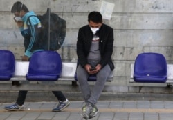 A man wearing a face mask to protect against the coronavirus sits at a bus stop in Tehran.