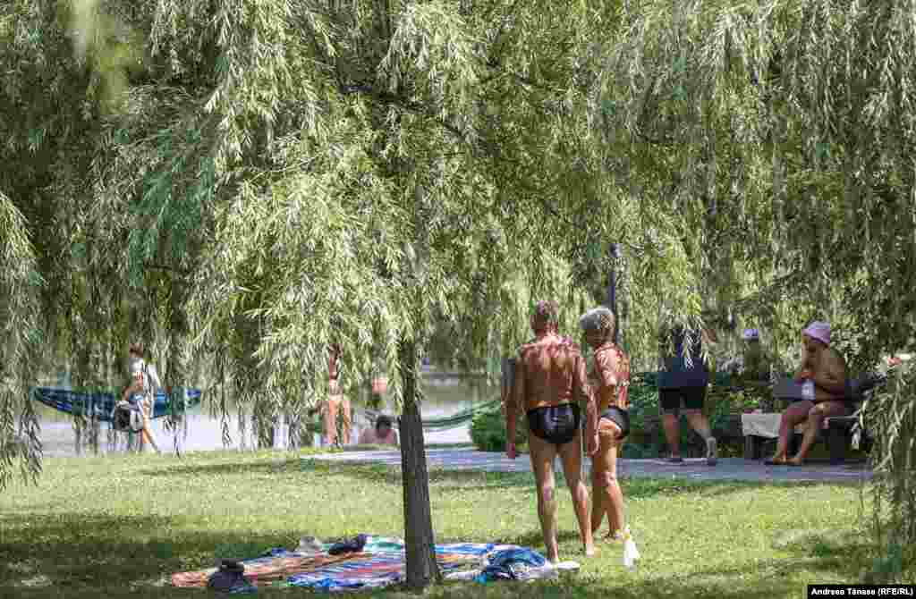 Mai multe persoane fac plajă lângă lacul din Parcul Alexandru Ioan Cuza din București.&nbsp;