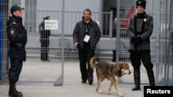 A Cossack (right) and a police officer (left) stand guard outside Sochi's main train station as a dog passes on January 17, with security measures already tight ahead of the Winter Olympics scheduled to begin on February 7.