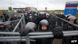 Slovenian policemen behind a fence as migrants and refugees cross the Croatia-Slovenia border in Trnovec on October 19.