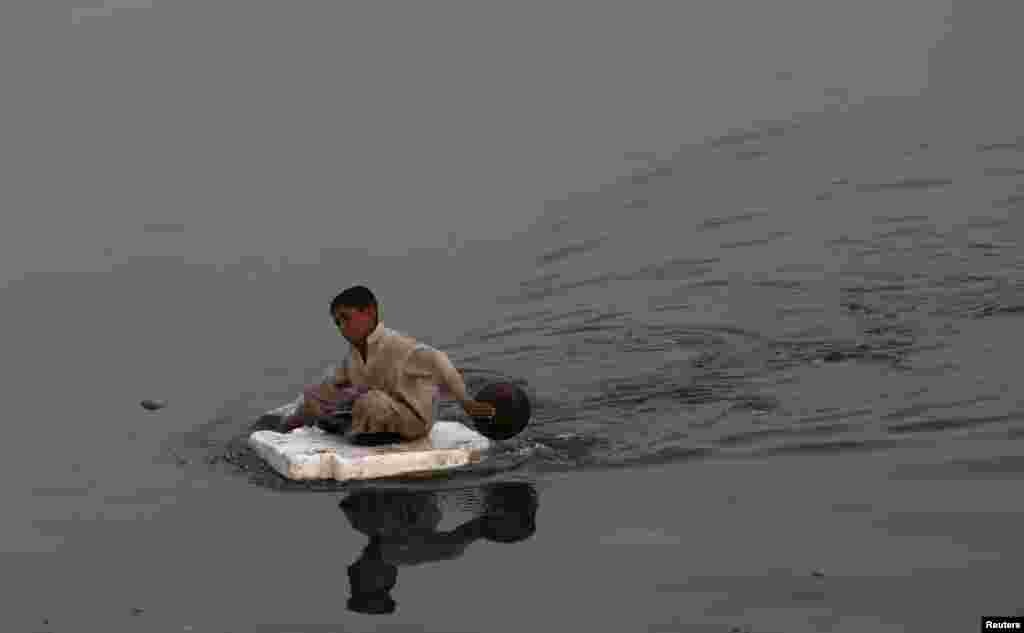 A boy sits on a piece of Styrofoam while searching for recyclables at China Creek in Karachi, Pakistan. (Reuters/Akhtar Soomro)