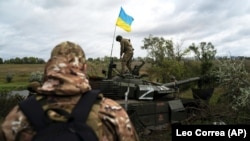 Украинский военный стоит на подбитом российском танке в Харьковской области, 19 сентября 2022 года. 