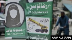 PAKISTAN -- A Pakistani man rides his bicycle past an election poster Sunni Muslim hardliner Tehreek-e-Labbaik Ya Rasool Allah (TLYRA) party depicting a female candidate in black scarf not showing her face, who is contesting for a parliamentary seat in th