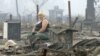 A woman sits surrounded by the remains of her house in the village of Mokhovoye on July 30