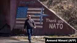 Një burrë duke ecur mbrapa mbishkrimit “Faleminderit NATO” dhe "Faleminderit SHBA", si dhe flamurit amerikan në Stagovë, vendbanim në Kaçanik, Kosovë.