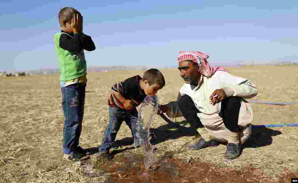 Syrian refugees drink water from a hose at the Syrian-Turkish border near Sanliurfa, Turkey, on September 26. (epa/Sedat Suna)