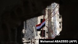 SYRIA -- The Syrian national flag rises in the midst of damaged buildings in Daraa-al-Balad, an opposition-held part of the southern city of Daraa, on July 12, 2018. 