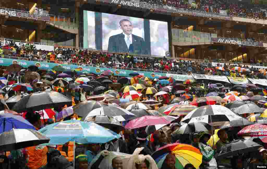 South Africans listen in the rain to U.S. President Barack Obama, who praised Mandela as a &quot;giant of history.&quot;