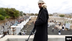 Вооруженный хусит охраняет похоронную процессию 25 мая 2015 г. после очередного налета саудовской авиации