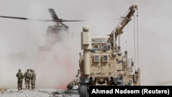 FILE: U.S. troops assess the damage to an armoured vehicle of NATO-led military coalition after a suicide attack in Kandahar province in August.