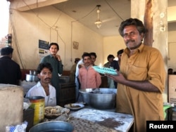 Chef (holding a plastic plate) at the Bhittai restaurant, Khorwah, in Sindh's Badin district. The village is lit by solar power.