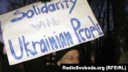 Участник акции солидарности с украинским народом стоит с плакатом у посольства Украины в Латвии.