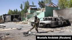 An Afghan soldier stands next to damaged army vehicles after a Taliban attack on the city (August, 2018).