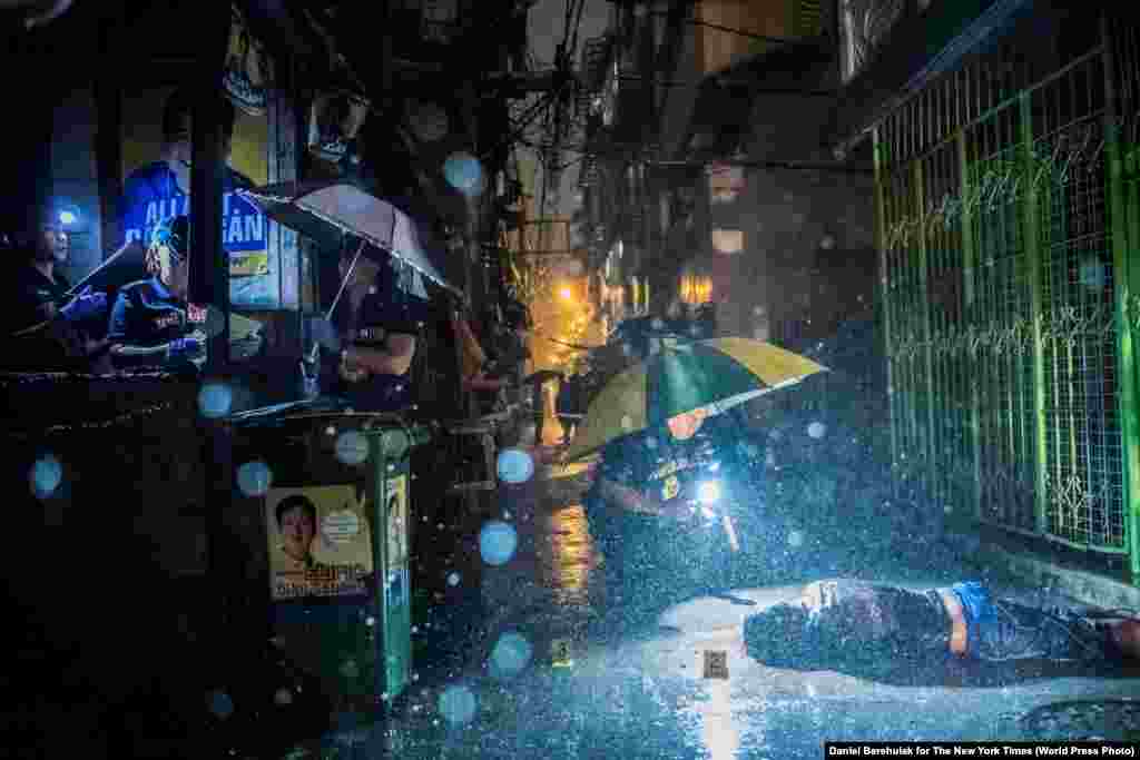 Heavy rain pours as police operatives investigate in an alley where 37-year-old Romeo Joel Torres Fontanilla was killed by two unidentified gunmen riding motorcycles in the early morning in Manila, Philippines. General News -- First Prize, Stories (Daniel Berehulak for The New York Times)