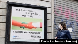 Žena prolazi pored plakata u Milanu sa rukama u bojama kineske i italijanske zastave na kojem piše "Neprijatelj je virus, ne narod. Napred, Kina" 10. marta 2020. godine