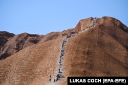 Tourists climb Uluru, Australia's iconic sandstone formation. Such activity is now banned.
