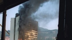 Поранешната зграда на парламентот се гледа како гори од уништен горен кат на хотелот „Холидеј ин“ во Сараево, откако беше погоденa од српски тенк на 19.09.1992 година.