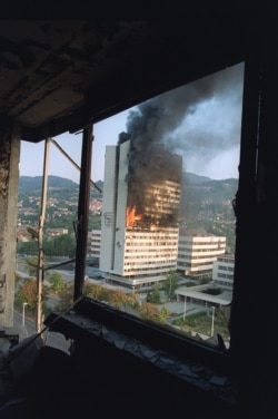 The Bosnian parliament building burns after being hit by Serbian tank fire, as seen from the destroyed upper floor of the Holiday Inn Hotel in September 1992.