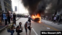 Участники протестов на фоне горящего полицейского автомобиля в Атланте. 29 мая 2020 года.