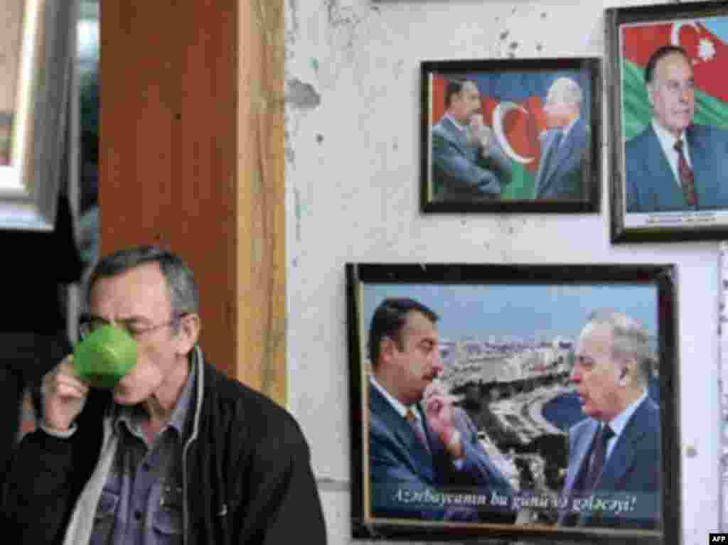 AZERBAIJAN, Baku : A man drinks from a mug near portraits of late Azeri President Heidar Aliyev and his son, current President Ilham Aliyev, in Baku on October 14, 2008. Ilham Aliyev is likely to sweep re-election for a second term on October 15 as the leader of oil-rich Azerbaijan, located in the turbulent Caucasus mountain zone. The opposition is boycotting the vote.