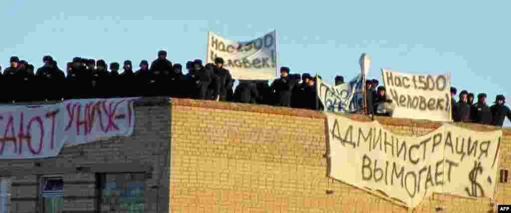 A group of inmates stands on a rooftop inside the prison. Two of the signs read, "We are 1,500 human beings!"