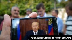 Președintele Putin vorbind la televiziune, reluat pe un smartphone 