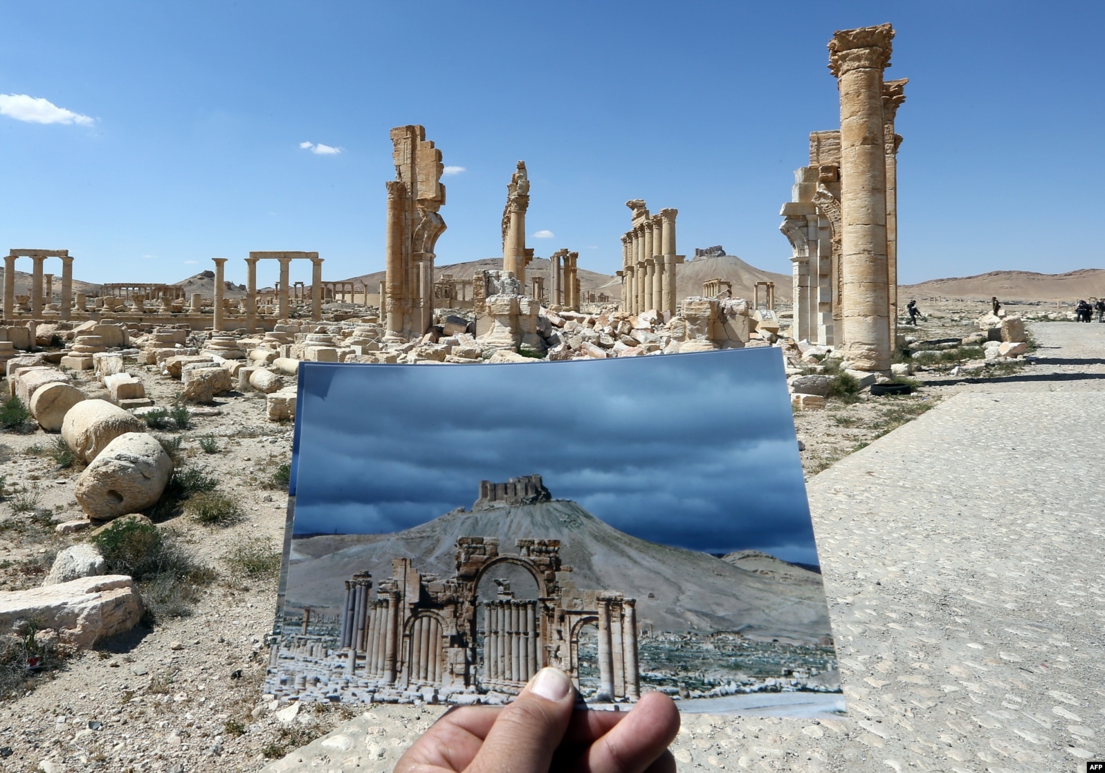 Fotograf drži svoju fotografiju Arc du Triomphe u Palmiri snimljenu 14. marta 2014. ispred ostataka povijesnog spomenika nakon što su ga militanti 