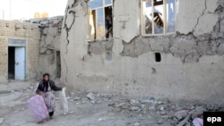 Iran -- An earthquake victim carries a few belongings as she walks next toa severly damaged house in the city of Varzeqan, north-western province of East Azerbaijan, 13Aug2012
