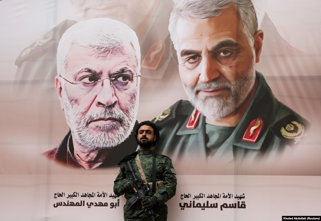 A Huthi militant stands by a poster of Iraqi militia commander Abu Mahdi al-Muhandis and Iranian military commander Qassem Soleimani during a rally by Huthi supporters to denounce the U.S. killing of both commanders, in Sanaa, Yemen, in 2020.