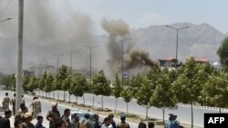 Afghan security personnel and bystanders look on as black smoke billows from the Afghan Parliament building in Kabul on June 22.